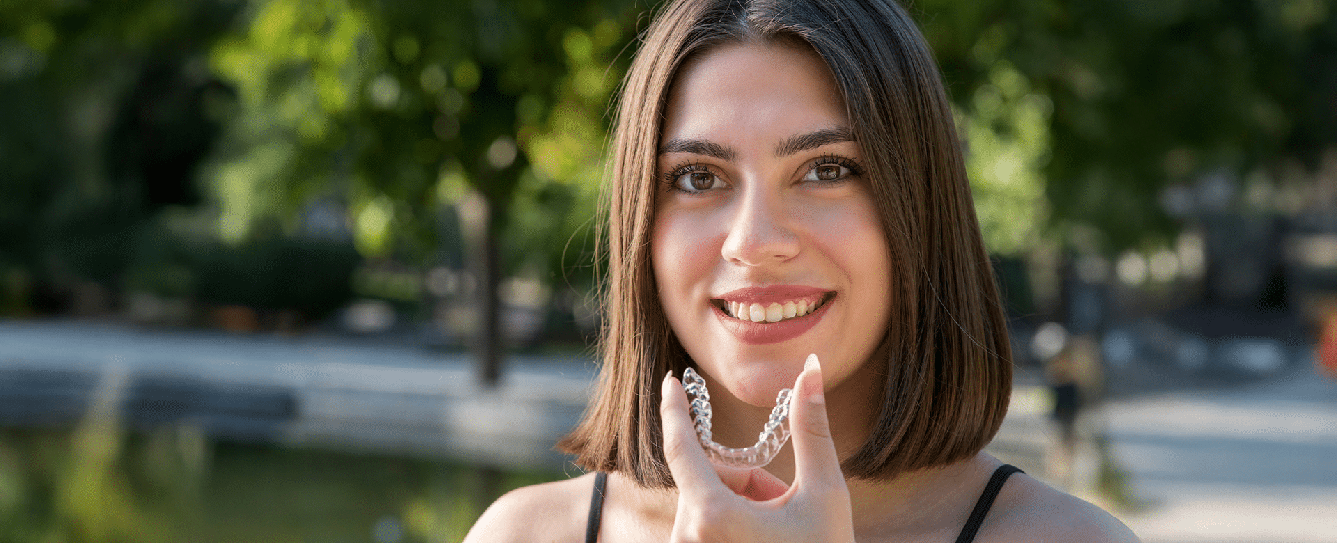 Girl smiling while holding an Invisalign aligner at Aura Dental Clinic, showcasing her dental treatment option.