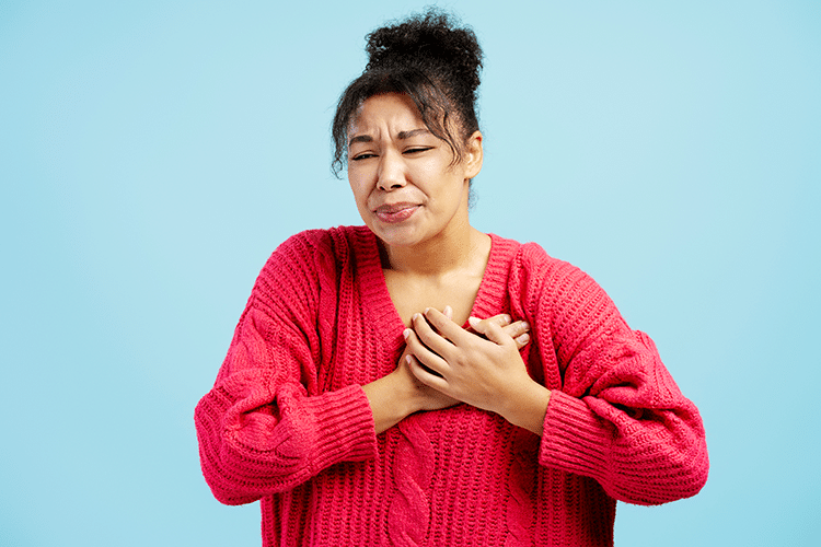 A woman in a pink sweater holds her chest, appearing distressed, in the context of Aura Dental Clinic.