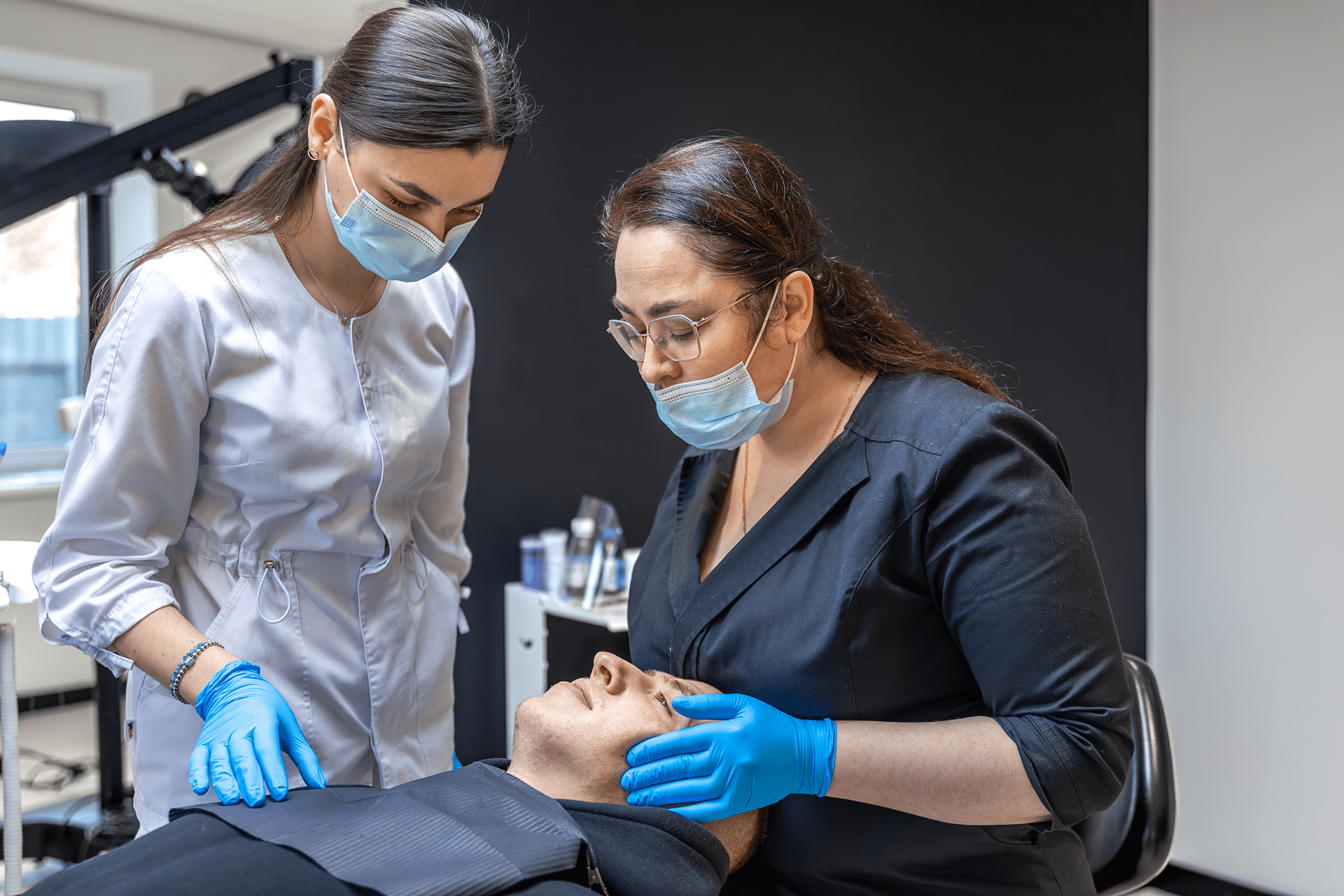 A woman wearing a mask in a dental office, with two dentists examining a patient at Aura Dental Clinic.