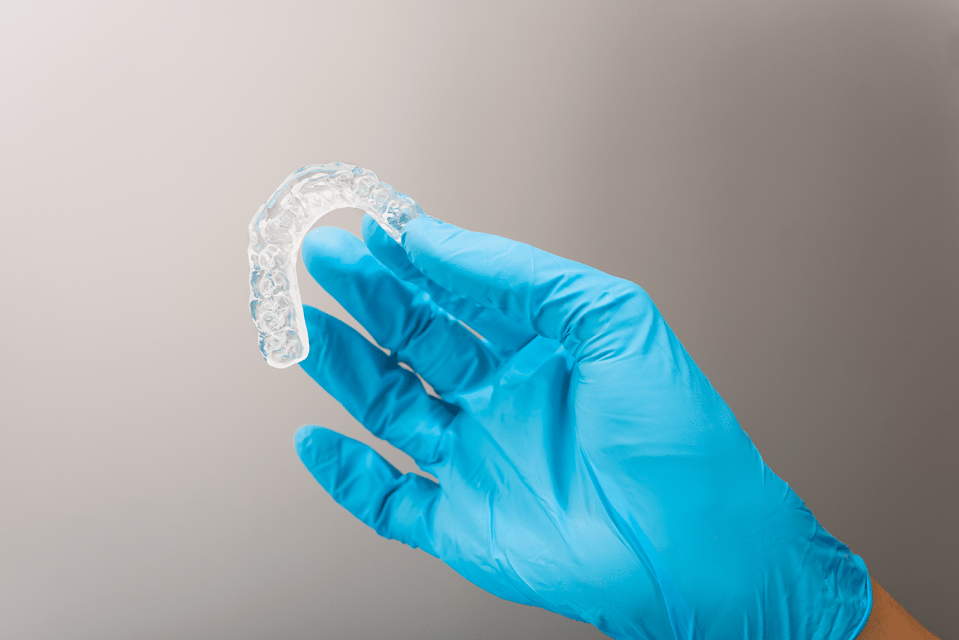 A hand wearing a blue glove holds a clear dental aligner.