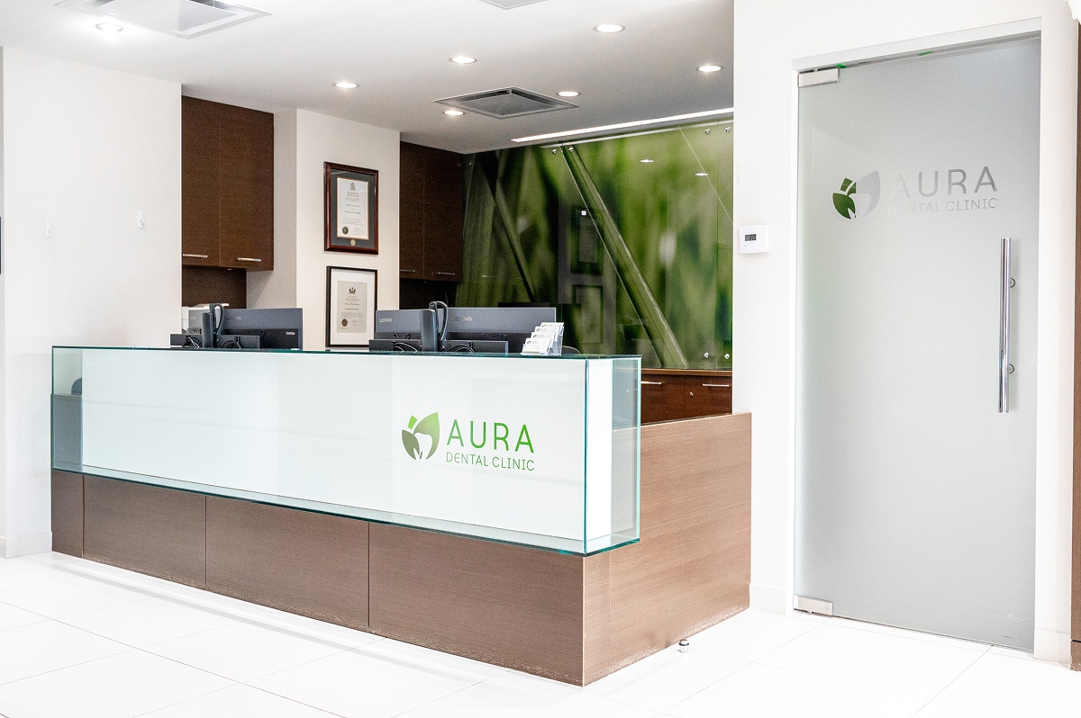 Reception desk at Aura Dental Clinic with a green plant on the wall, creating a welcoming atmosphere.