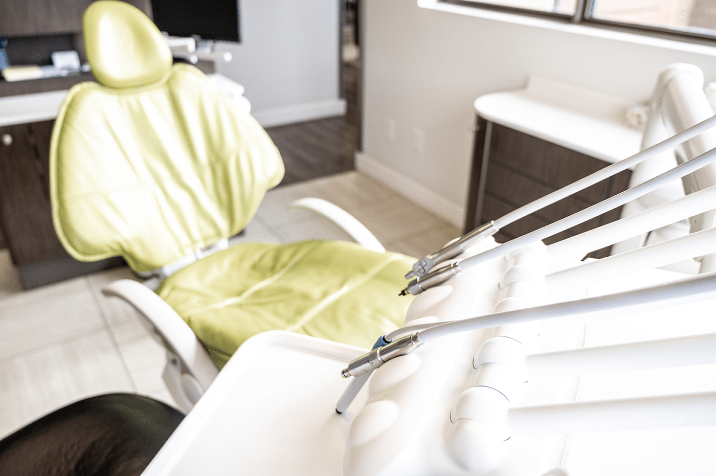 A dental chair in a bright office setting, with dental tools on a white countertop.