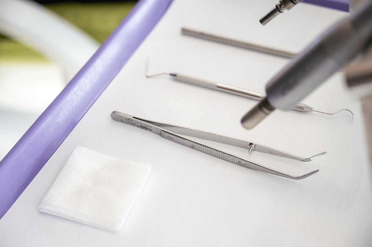 A dental tray with various dental tools, including tweezers, an explorer, and a cotton pad.