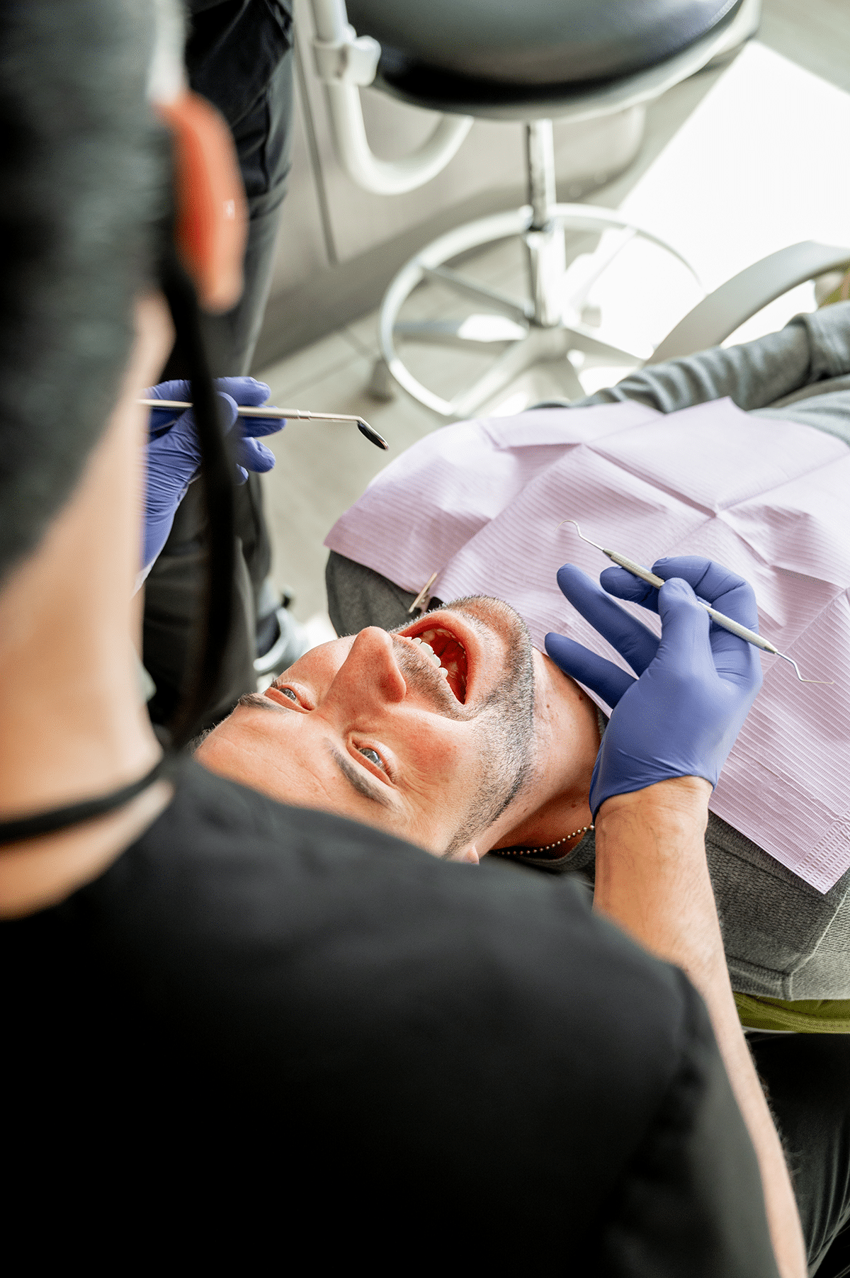 A dental professional is examining a patient lying in a dental chair, holding dental instruments while the patient has their mouth open.