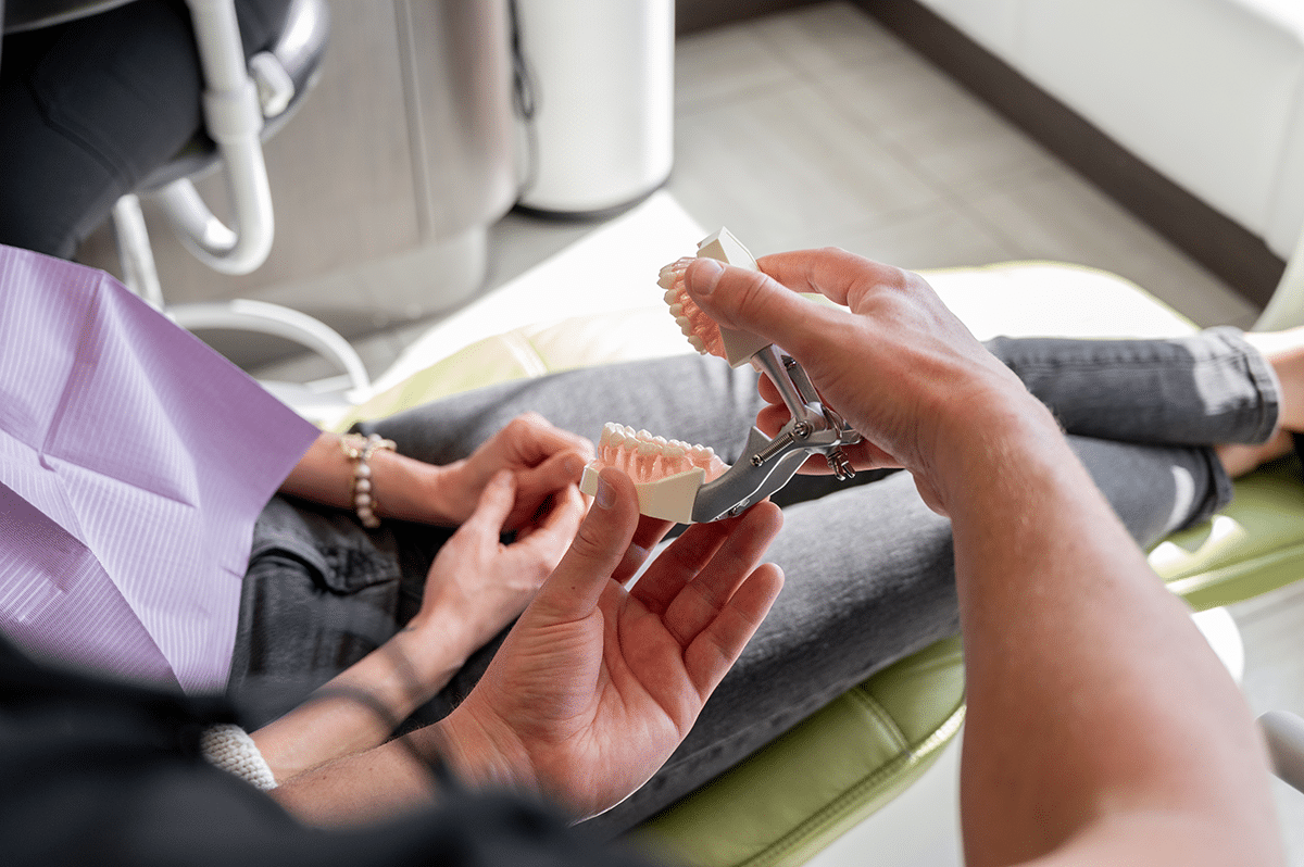 A dental professional is demonstrating the use of a dental model to a patient sitting in a dental chair.