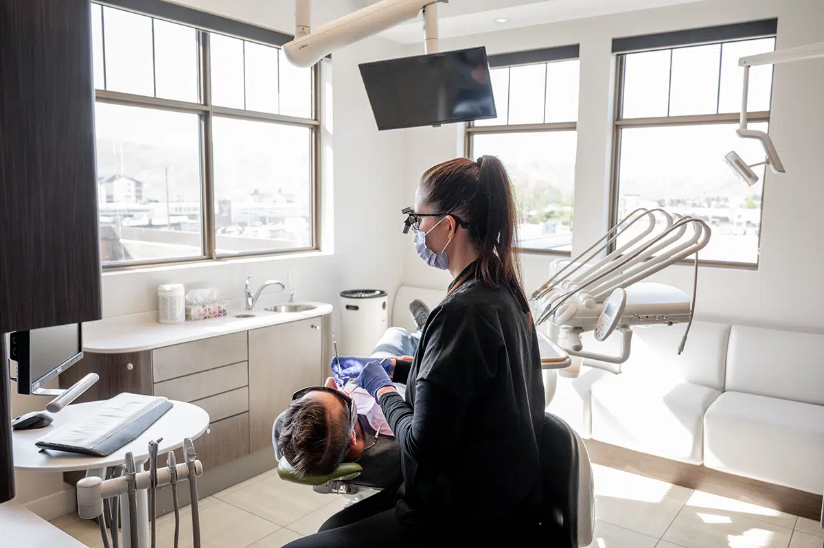 A dental hygienist wearing a mask and gloves is attending to a patient in a modern dental office.