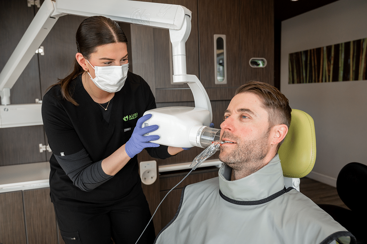 A dental professional wearing a mask and gloves is using equipment for a dental procedure on a seated patient.